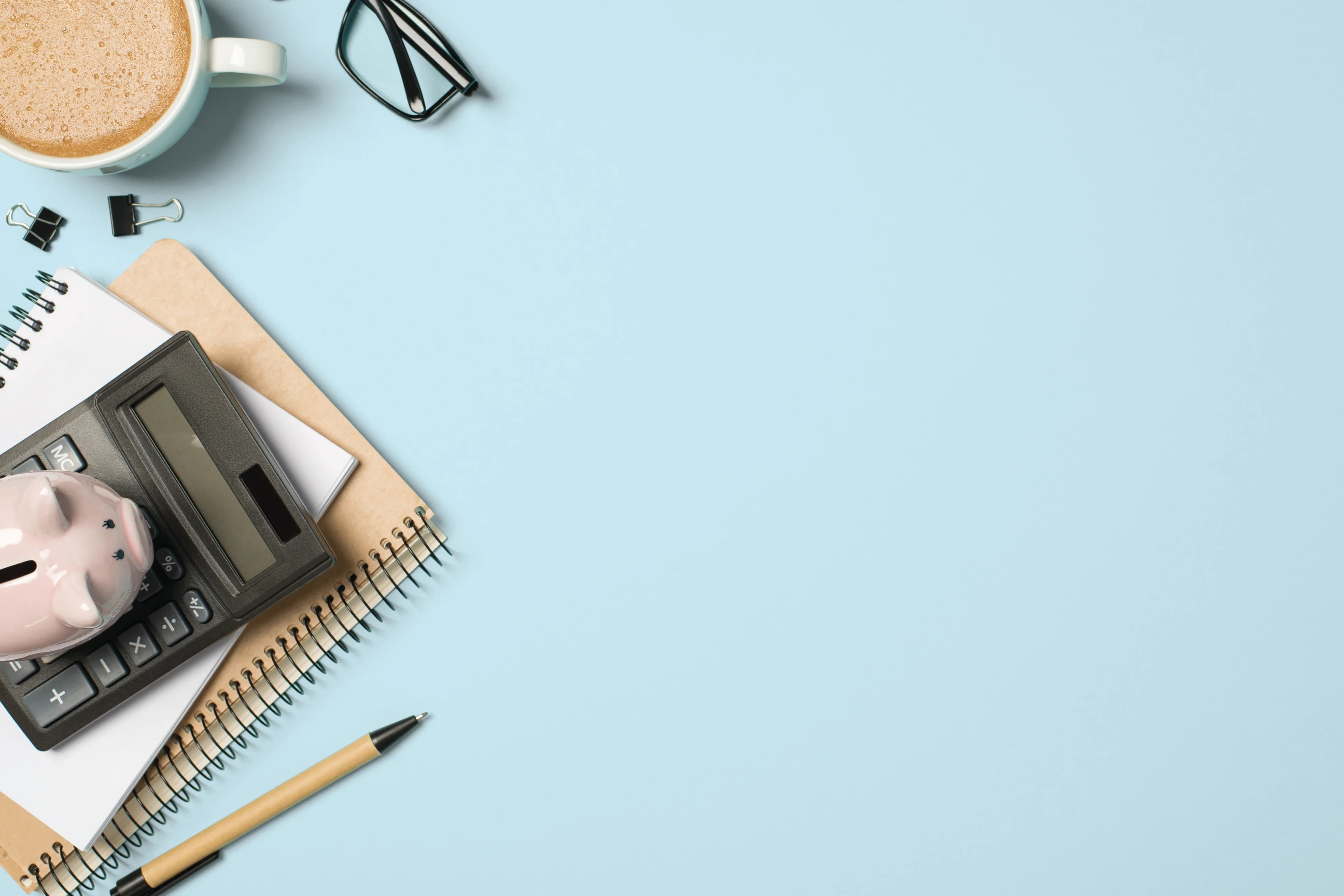 Calculator, piggy bank, notebook, pen, coffee and glasses on a blue background.