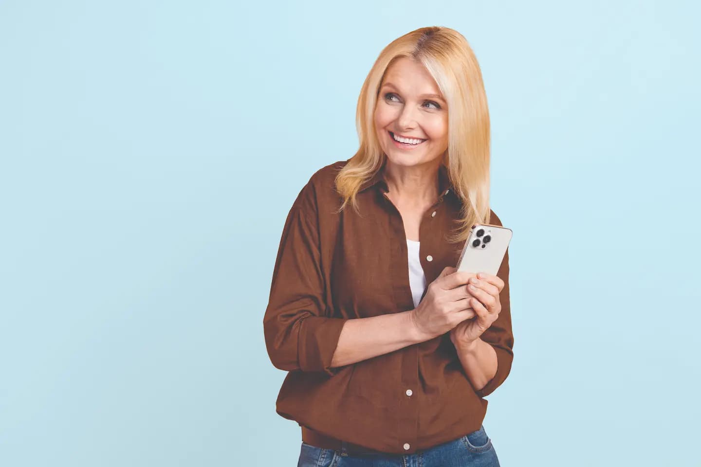 A woman smiling and holding a smartphone on a light blue background.